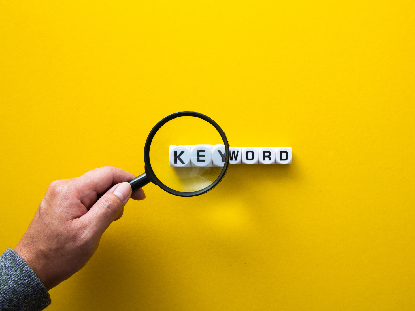 Magnifying glass highlighting the word 'keyword' on yellow background – concept for keyword research in SEO.