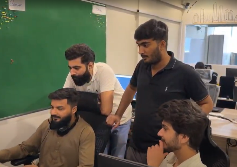 Four male team members collaborating closely in a modern, open-plan office.
